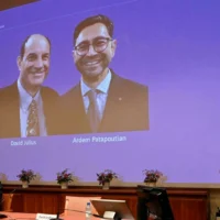 2021年10月4日、スウェーデン・ストックホルムのカロリンスカ研究所で行われた記者会見で、2021年のノーベル生理学・医学賞の受賞者デビッド・ユリウス（左）とアーデム・パタポウティアンが映し出されたスクリーンの横に立つ、ノーベル生理学・医学賞委員会委員のパトリック・エルンフォルス（右）。AFP-Jonathan Nackstrand