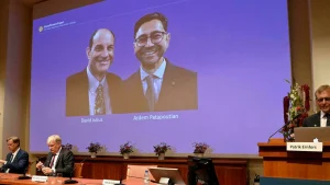 2021年10月4日、スウェーデン・ストックホルムのカロリンスカ研究所で行われた記者会見で、2021年のノーベル生理学・医学賞の受賞者デビッド・ユリウス（左）とアーデム・パタポウティアンが映し出されたスクリーンの横に立つ、ノーベル生理学・医学賞委員会委員のパトリック・エルンフォルス（右）。AFP-Jonathan Nackstrand