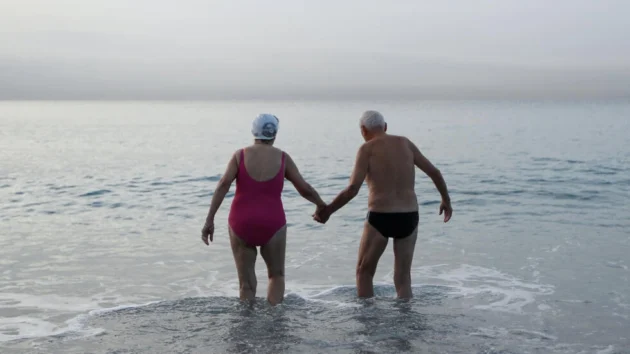 フランスのリビエラ市ニースの地中海に入ると、年配の男性と女性が手をつないでいる。© AFP / ヴァレリー・ハチェ